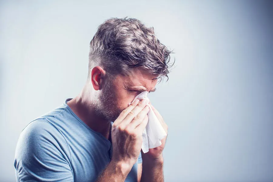 Allergies-Doctor A man in a gray shirt blows his nose. Get help for allergies from Dr. Robert Powers of Eternal Vitality Orlando in Orlando.