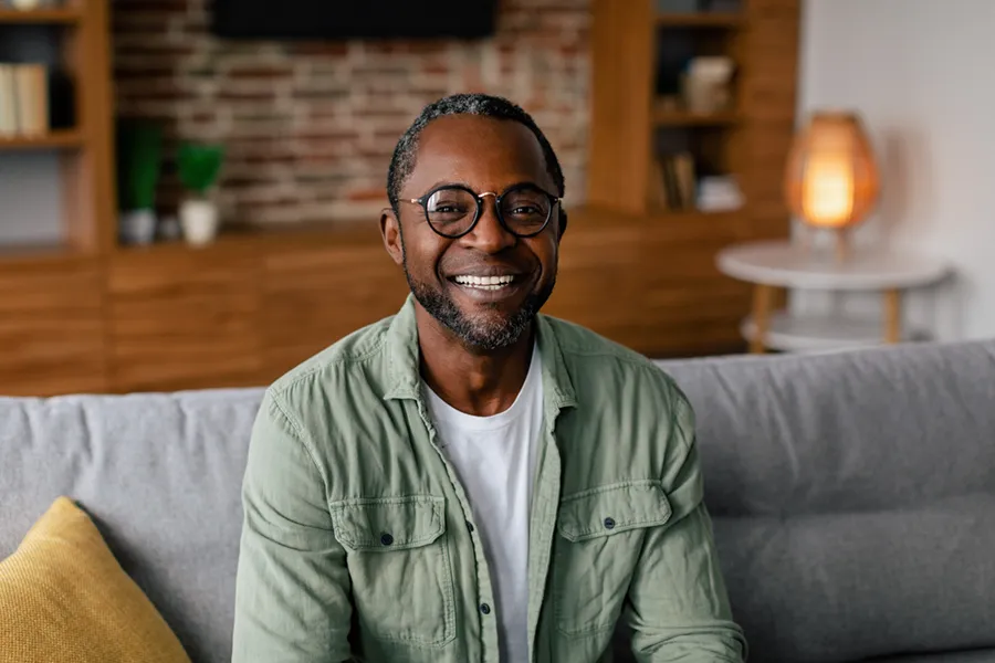 Andropause-Doctor A middle aged black man in a green button up shirt sits on his couch smiling, happy with his treatment for andropause and low testosterone from Dr. Robert Powers of Eternal Vitality Orlando in Orlando.