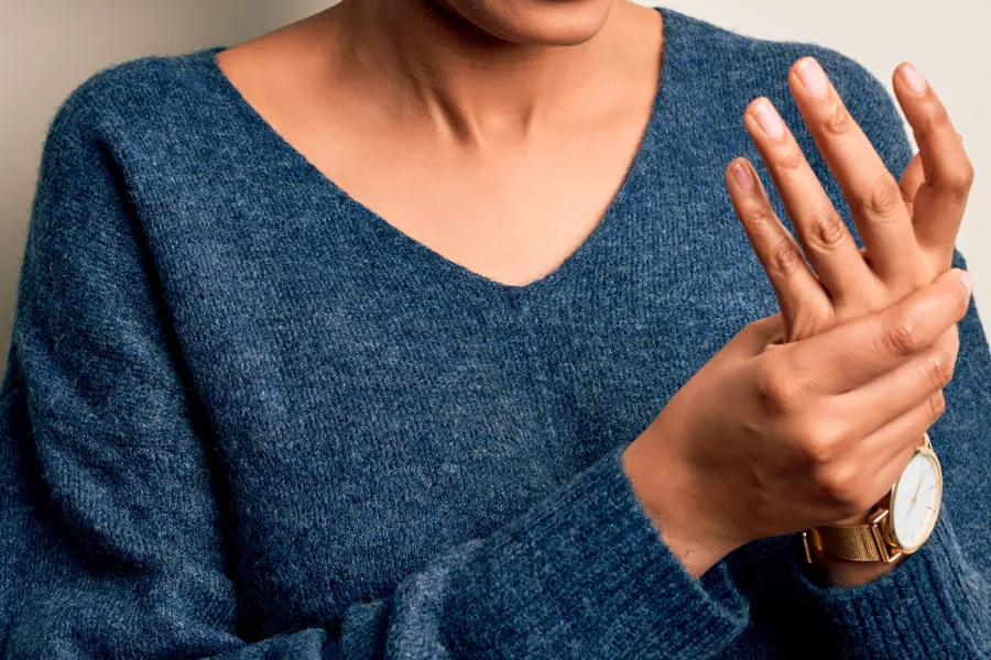 Arthritis-Doctor Close up of a woman in a blue sweater massaging one aching hand with the other. Get help for arthritis from Dr. Robert Powers of Eternal Vitality Orlando in Orlando.