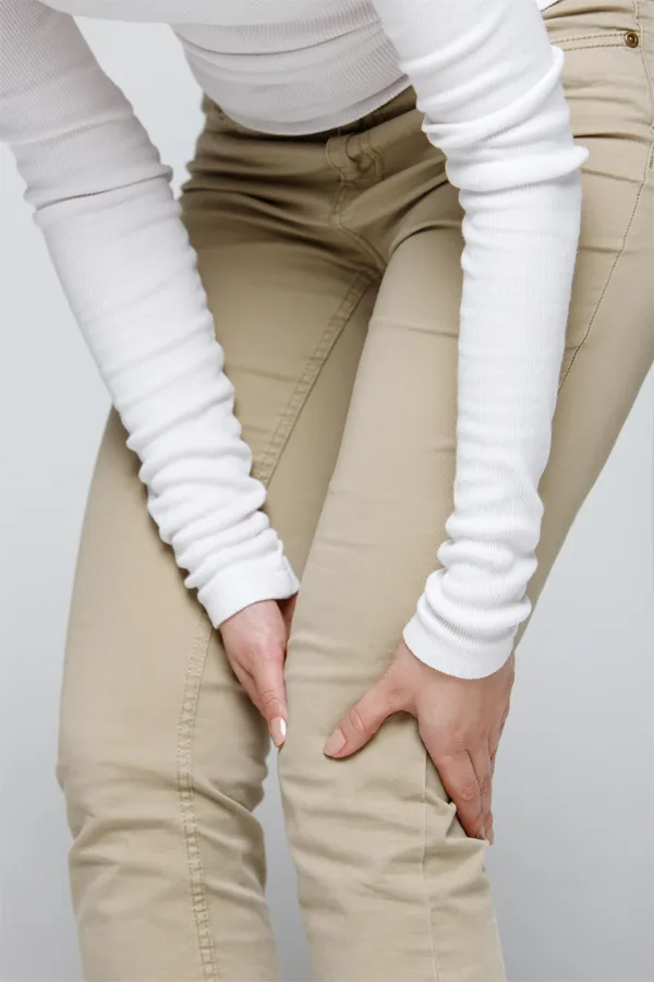Arthritis-Treatment A woman wearing a white long-sleeve shirt and tan pants, clutching her knee, suffering from arthritis. Get arthritis treatment from Dr. Robert Powers of Eternal Vitality Orlando in Orlando.