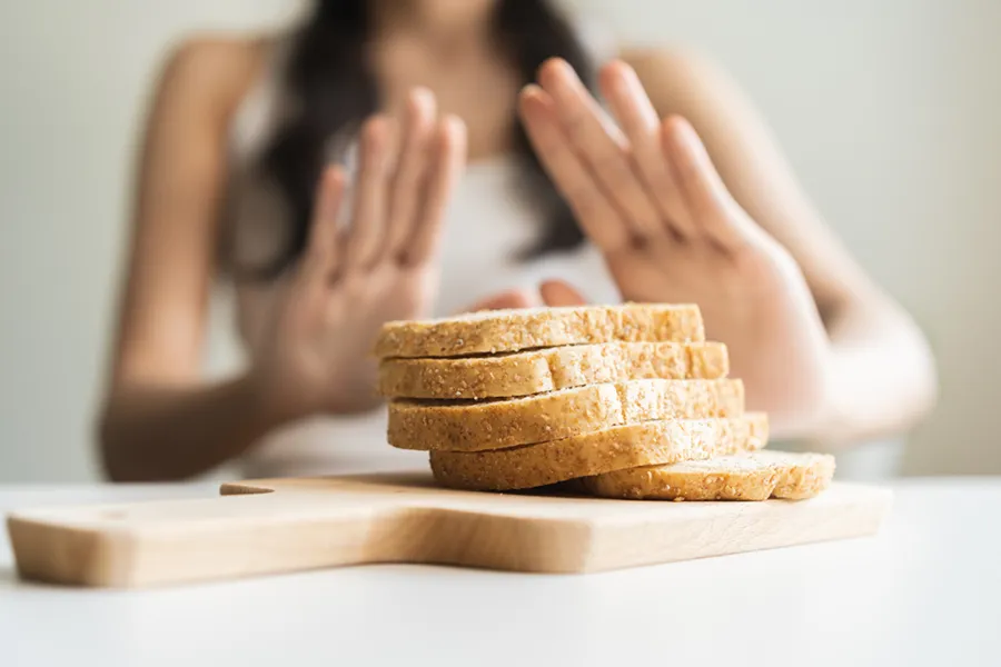 Celiac-Disease-Clinic Close up of a stack of bread slices on a cutting board with a woman's hands behind them, refusing to eat. Get treatment for Celiac Disease from Dr. Robert Powers of Eternal Vitality Orlando in Orlando.