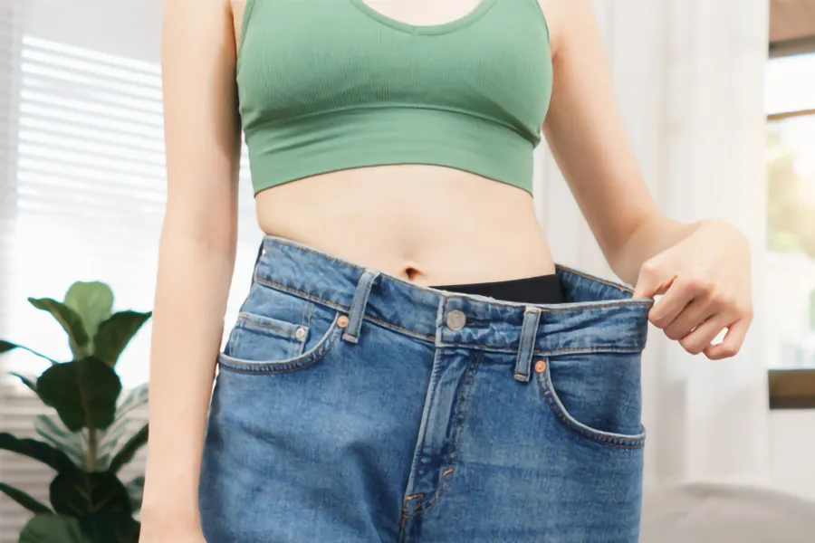 Electric-Muscle-Stimulation-Body-Sculpting-Clinic A woman pulls her jeans away from her waist to show her weight loss. Get Electric Muscle Stimulation (EMS) Body Sculpting treatments from Dr. Robert Powers of Eternal Vitality Orlando in Orlando.
