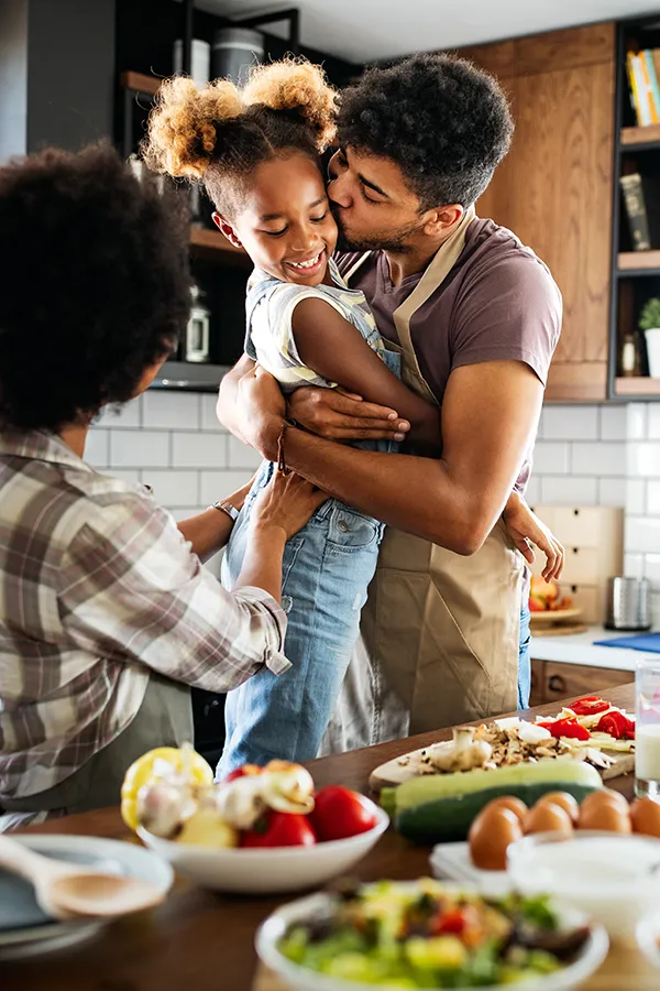 Gut-Health-Treatment A man holds his daughter and kisses her cheek as the family makes a healthy dinner in the kitchen. Get help for digestive issues and gut health from Dr. Robert Powers of Eternal Vitality Orlando in Orlando.