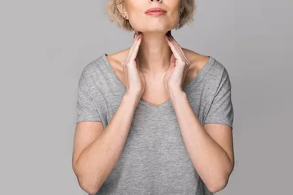 Hashimotos-Thyroiditis-Doctor An older blonde woman in a gray t-shirt holds her hands to her neck checking for signs of thyroid problems. Get help for Hashimoto's Thyroiditis from Dr. Robert Powers of Eternal Vitality Orlando in Orlando.