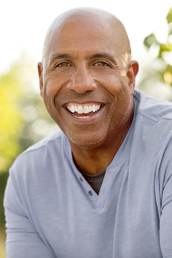 Healthy-Aging-Peptides-Treatment A middle-aged black man in a gray v-neck t-shirt sits outside smiling, happy with the healthy aging peptide treatments from Dr. Robert Powers of Eternal Vitality Orlando in Orlando