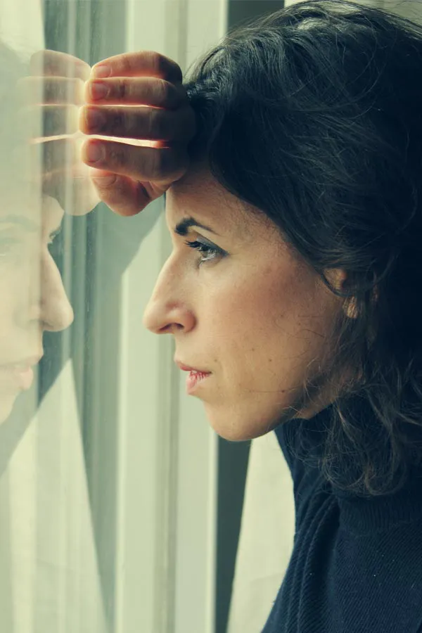 PCOS-Treatment A brunette woman in a thin dark turtleneck looks out the window with a serious expression, suffering from PCOS. Get treatment for Polycistic Ovarian Syndrome/PCOS from Dr. Robert Powers of Eternal Vitality Orlando in Orlando.
