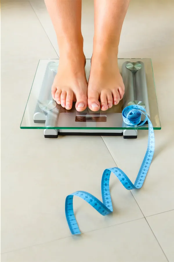 Weight-Loss-Resistance-Treatment Close-up of a woman's feet standing on a scale, with measuring tape by her toes, getting treatment for weight loss resistance from Dr. Robert Powers of Eternal Vitality Orlando in Orlando.
